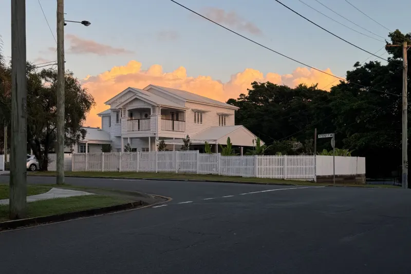 Holland House, a renovated white two-storey Queenslander with a picket fence in Kedron, at sunset